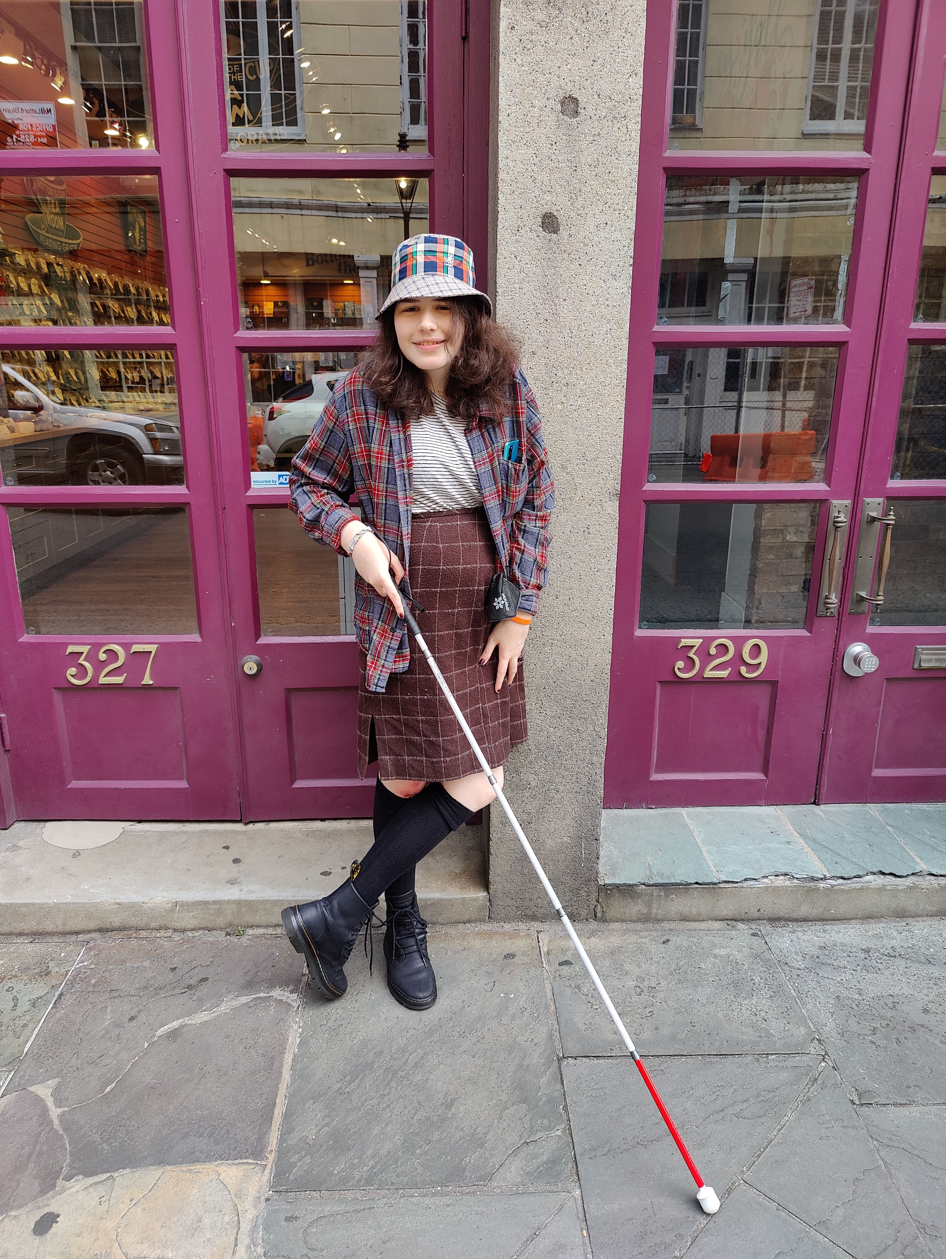 A Picture of me standing on a new-orleans street corner. I'm wearing a plaid shirt and skirt, knee-high stockings, and a cool new bucket hat!